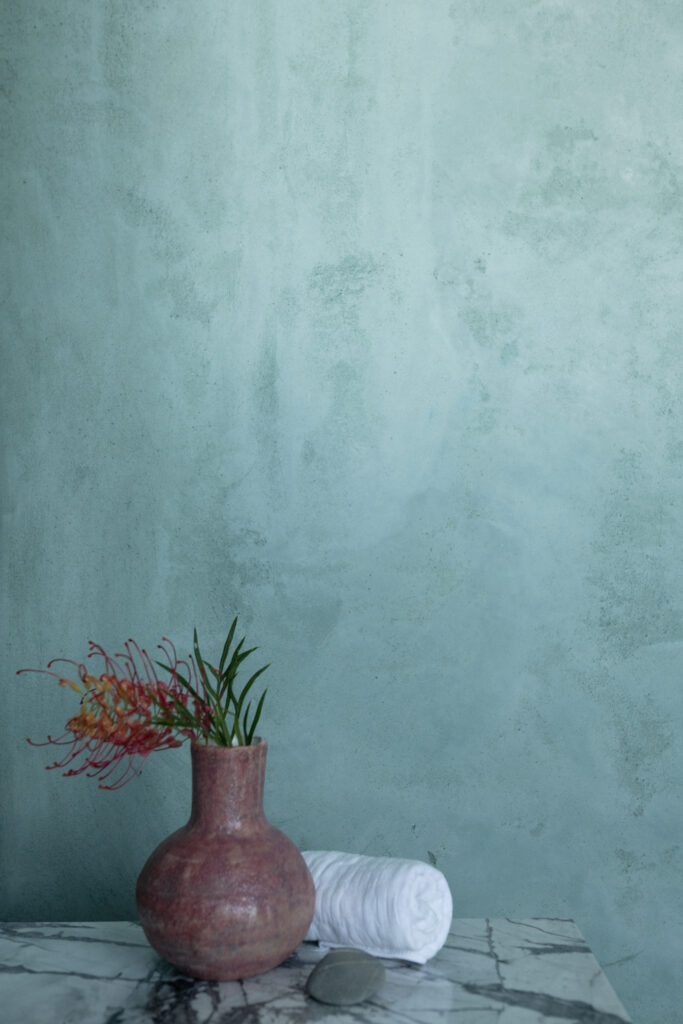 hand made ceramic vase with native flower  infront of green plastered wall in a bathroom