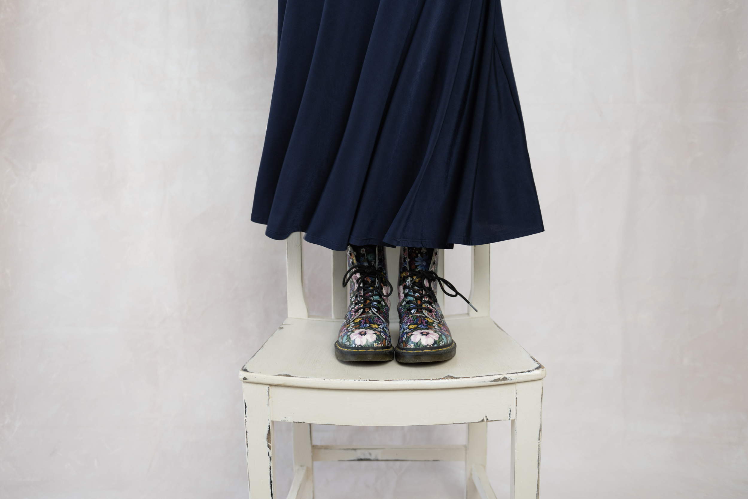 Woman dancing on chair with only her flowery boots visible beneath her swaying skirt.